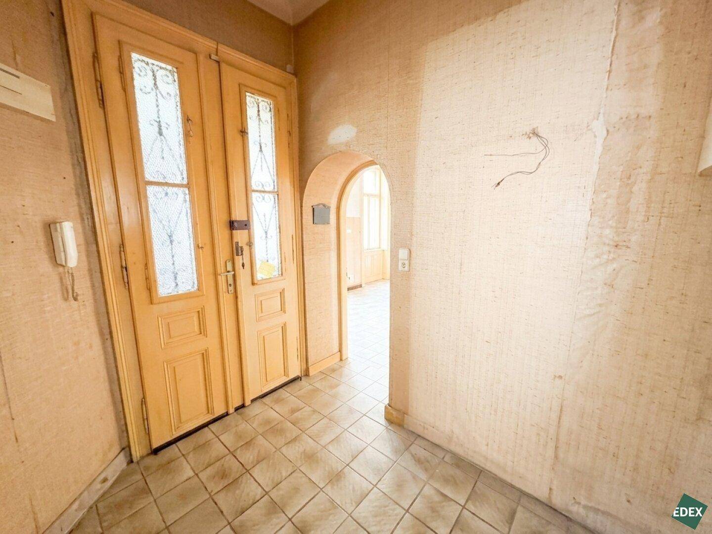 Eingangsbereich mit doppelter Holztür, Fliesenboden und einem Rundbogen zu weiteren Räumen.