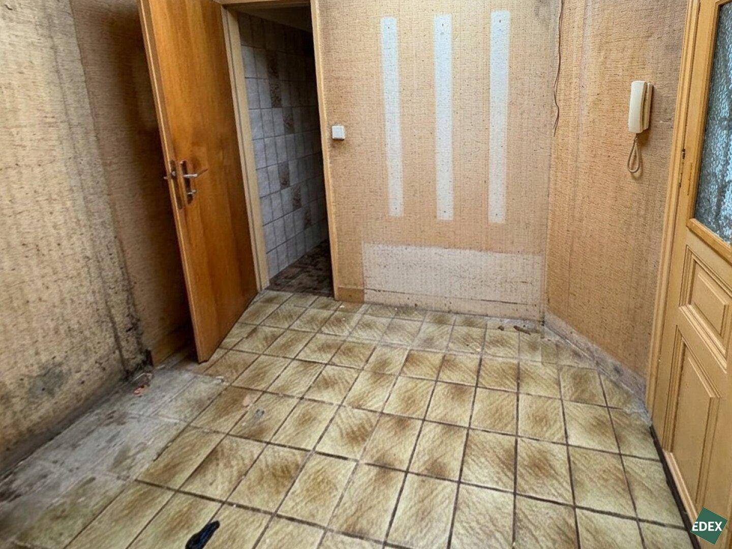 Flur mit Fliesenboden und einer Tür, die zu einem weiteren Bereich führt.