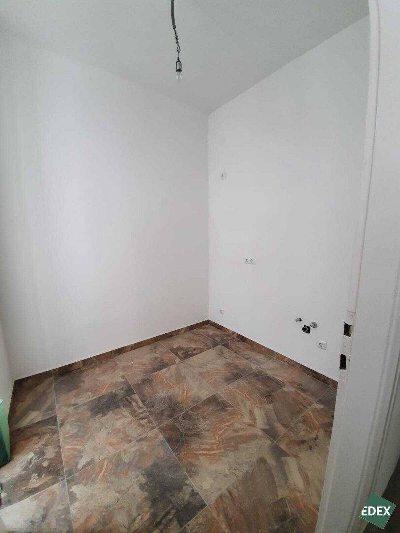 Leerer Raum mit Fliesenboden und Anschlüssen für eine Küche, bereit für den Einbau.