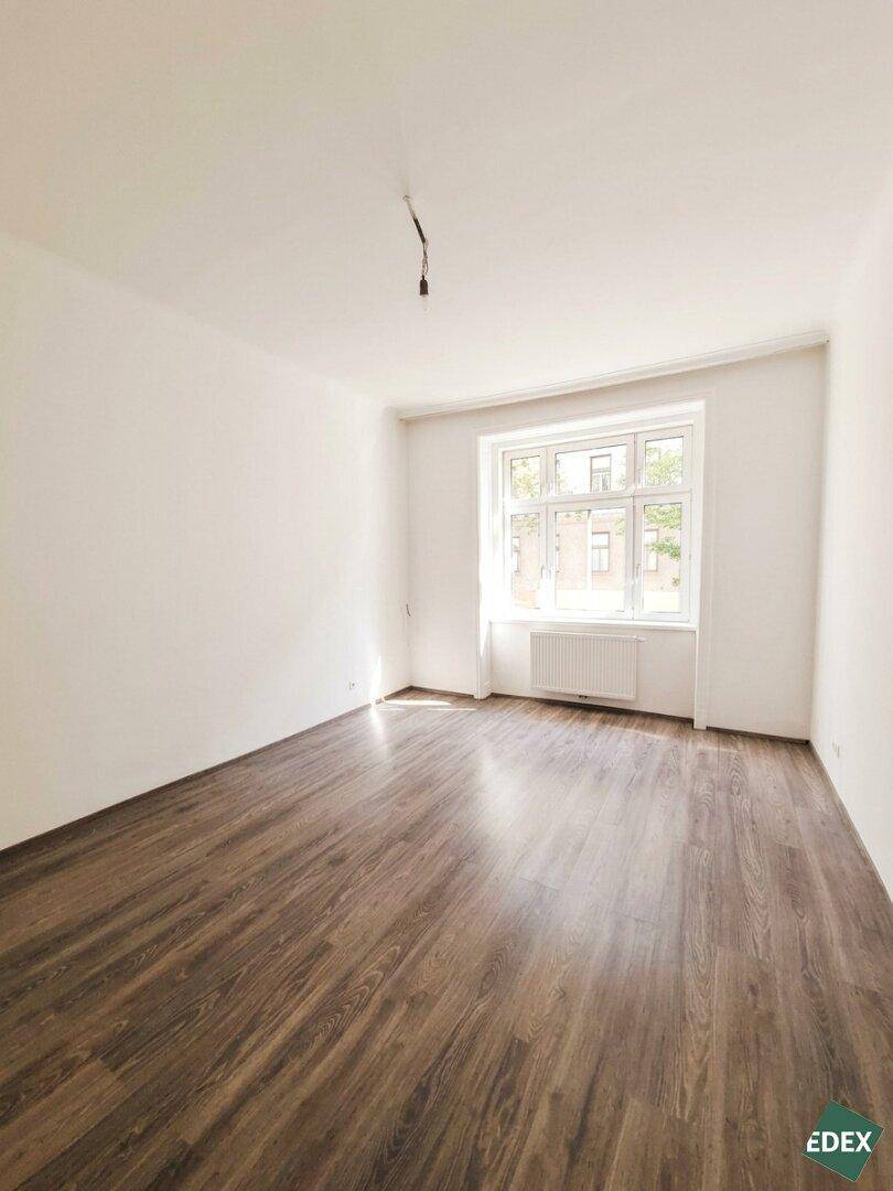 Geräumiges, unmöbliertes Zimmer mit Laminatboden und einem großen Fenster, das viel Licht hereinlässt.