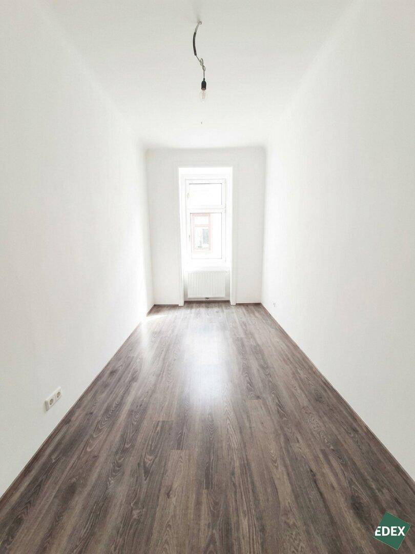Langes, schmales Zimmer mit Laminatboden und einem Fenster am Ende, ideal für verschiedene Nutzungen.