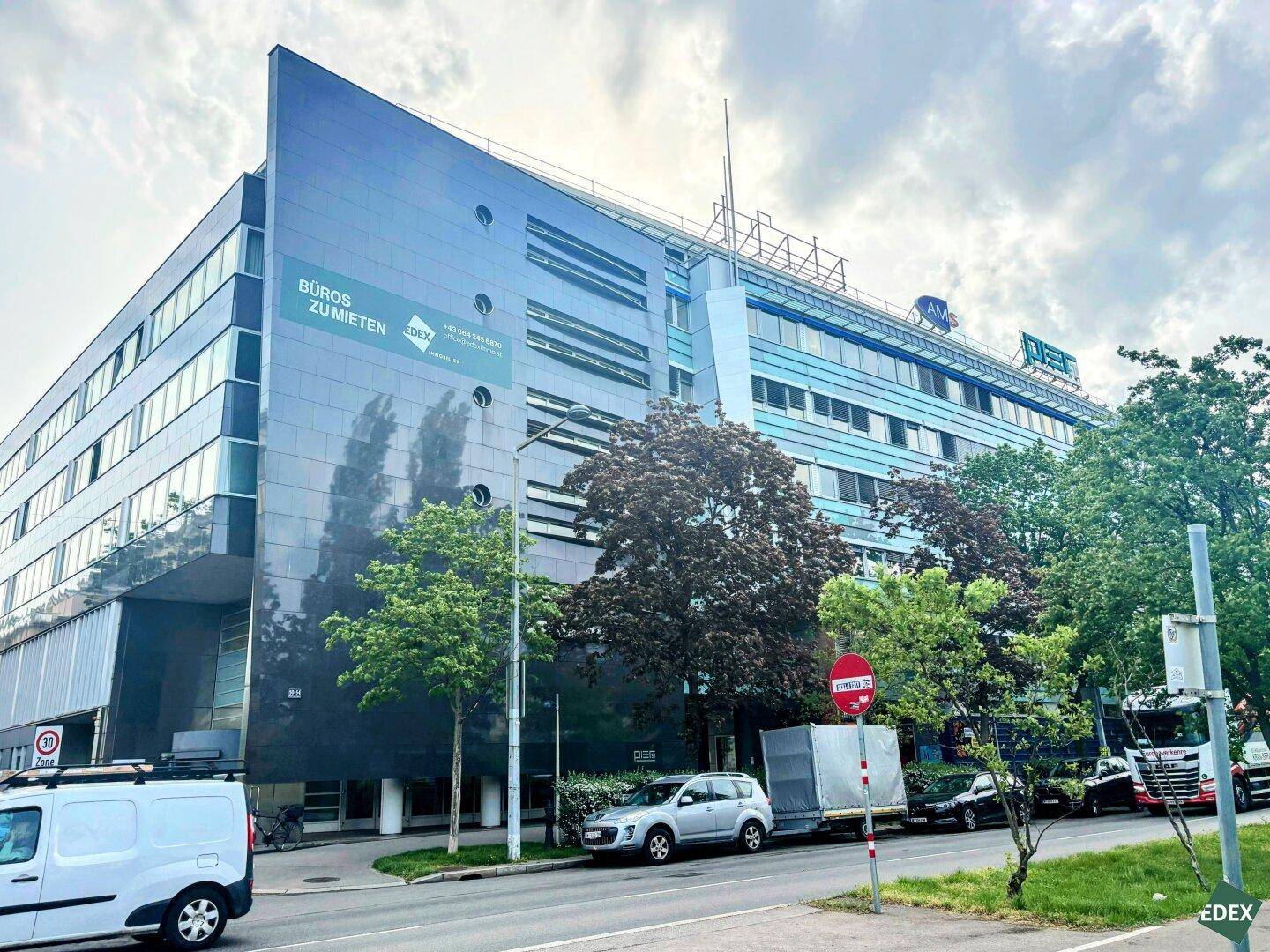 Modernes Bürogebäude mit Glasfassade und Werbeschildern an einer belebten Straße.