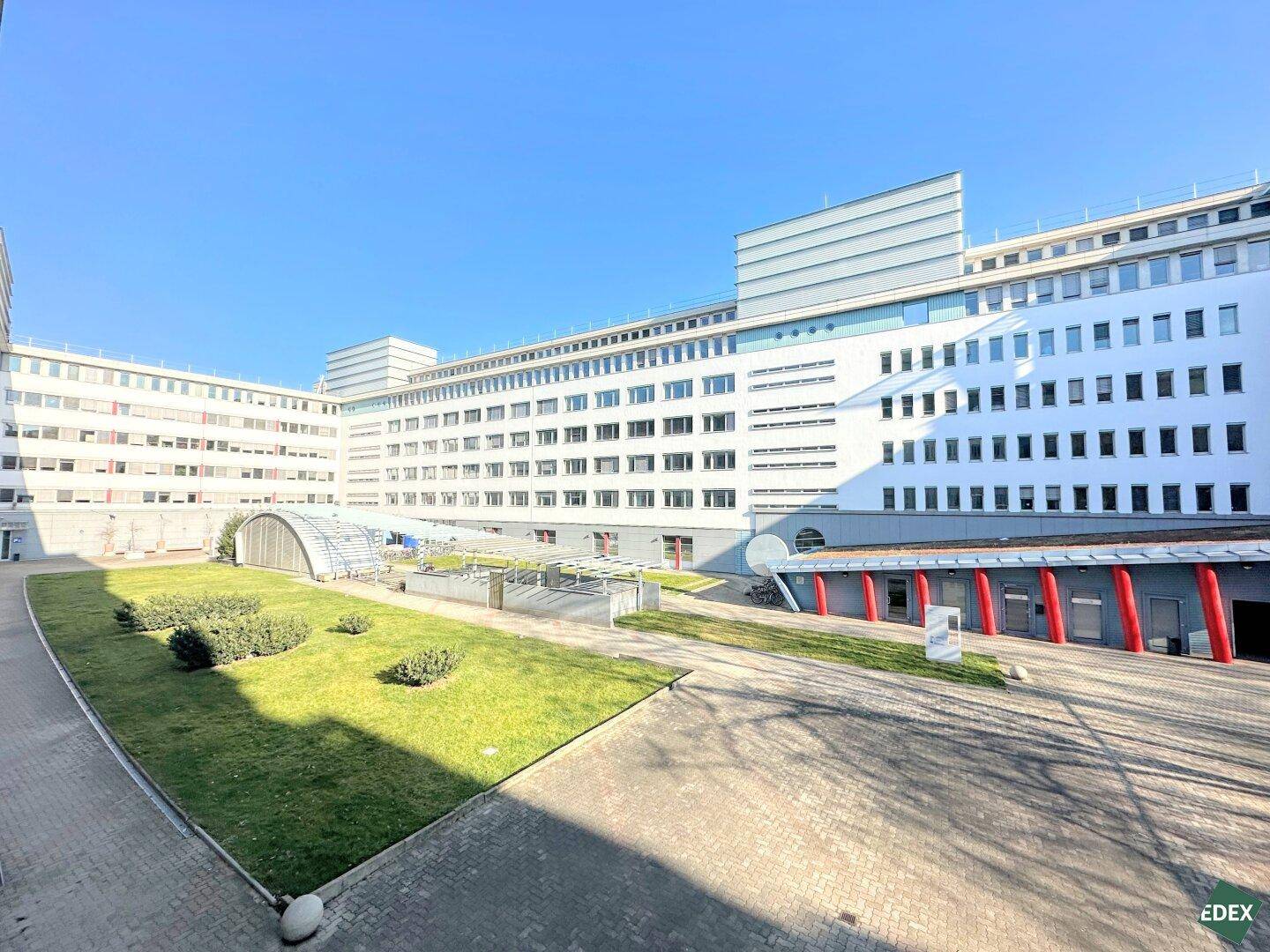 Großer Gebäudekomplex mit einem gepflegten Innenhof und Grünflächen unter blauem Himmel.