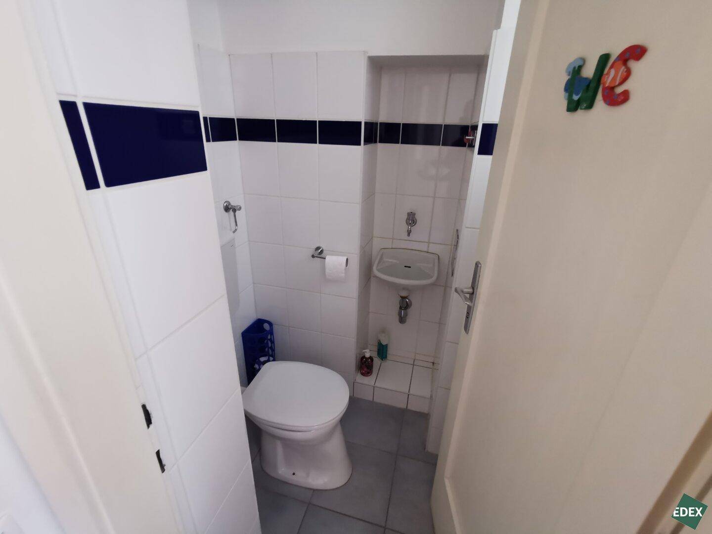 Kleines separates WC mit Waschbecken und weißen Fliesen, funktional eingerichtet.