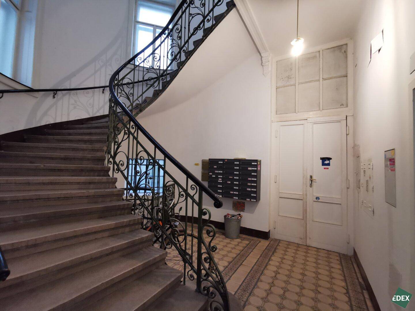 Elegantes Treppenhaus mit geschwungenem Geländer und Marmorstufen in einem Altbau.