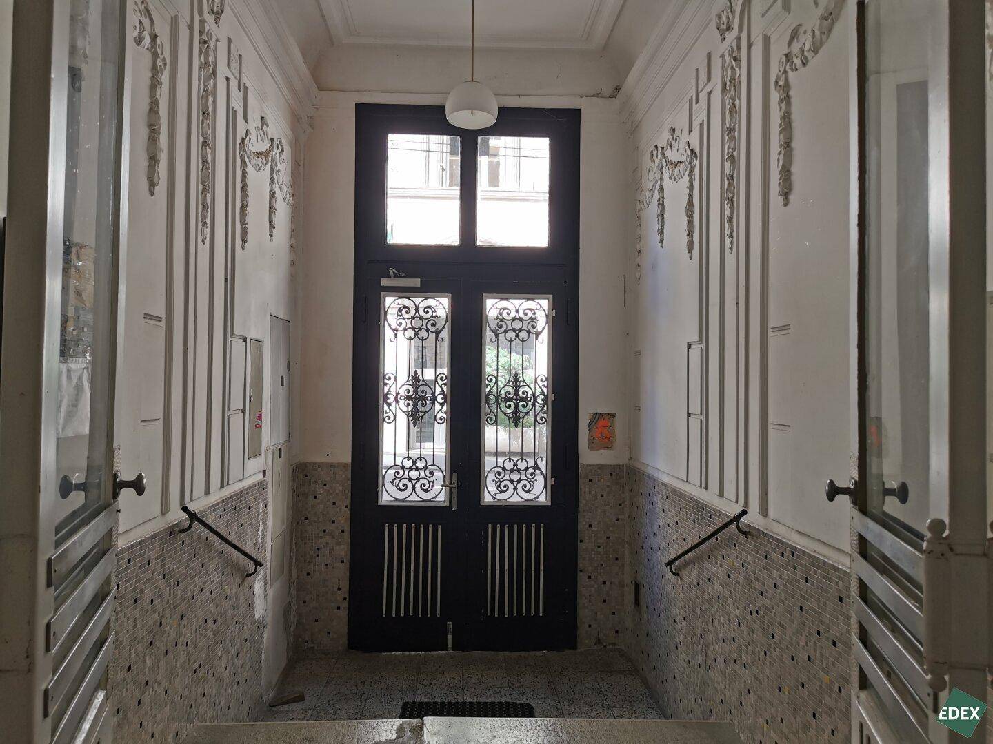 Historischer Eingangsbereich mit verzierten Wänden, Mosaikfliesen und einer Doppeltür.