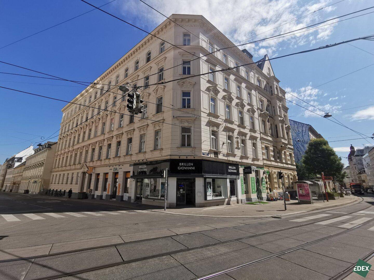 Historisches Eckgebäude mit vielen Fenstern und Geschäften im Erdgeschoss an einer belebten Kreuzung.