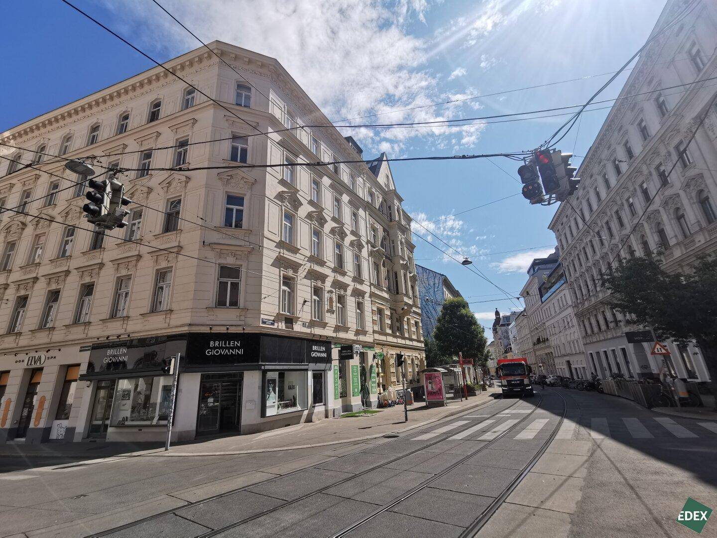 Historisches Gebäude an einer städtischen Kreuzung mit Geschäften und Straßenbahnschienen.