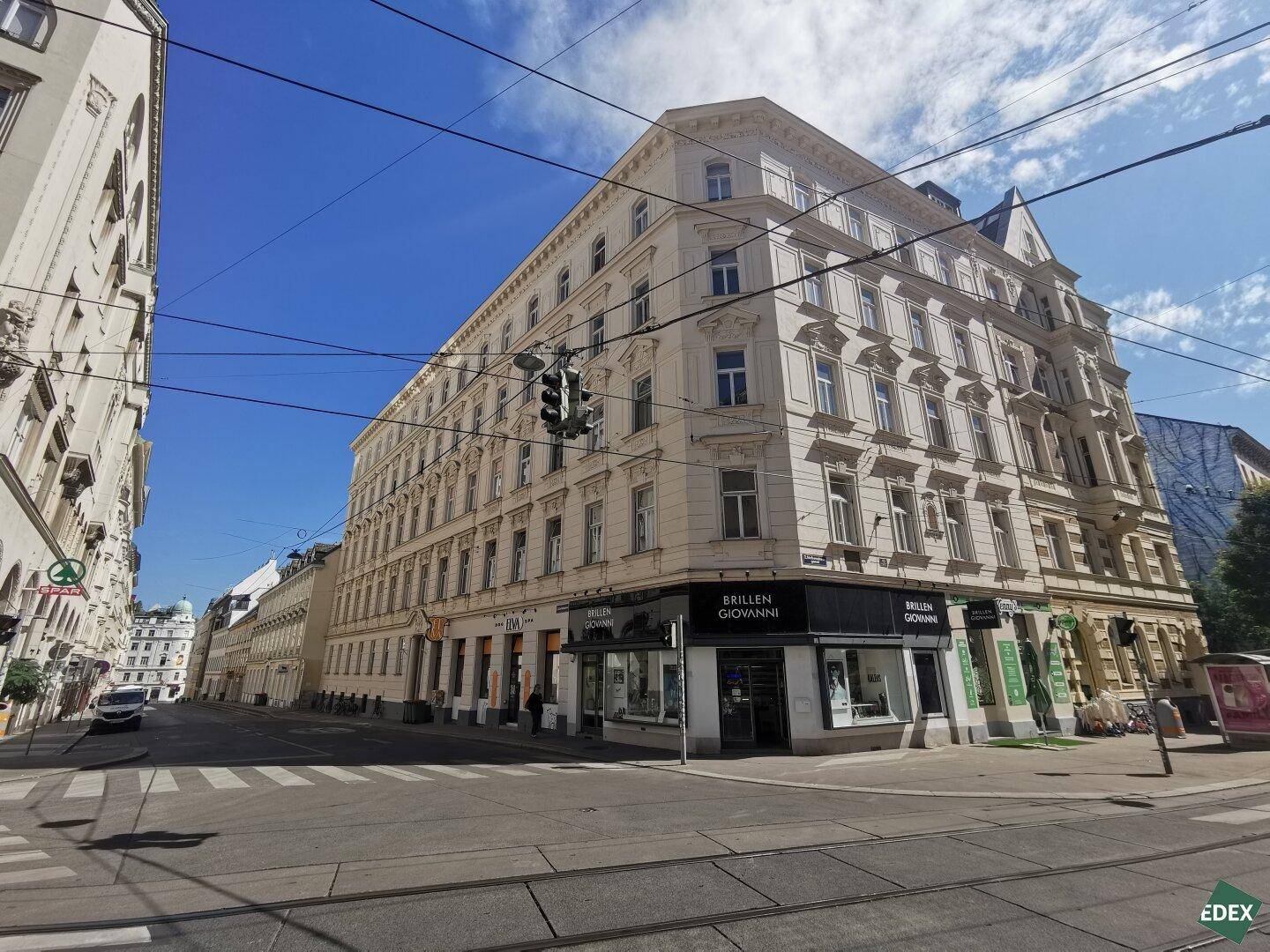 Großes Eckgebäude mit klassischer Architektur und Geschäften im Erdgeschoss unter blauem Himmel.