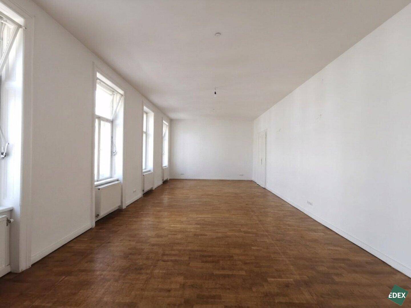 Langer, heller Raum mit Holzboden und einer Reihe von Fenstern entlang der Wand.