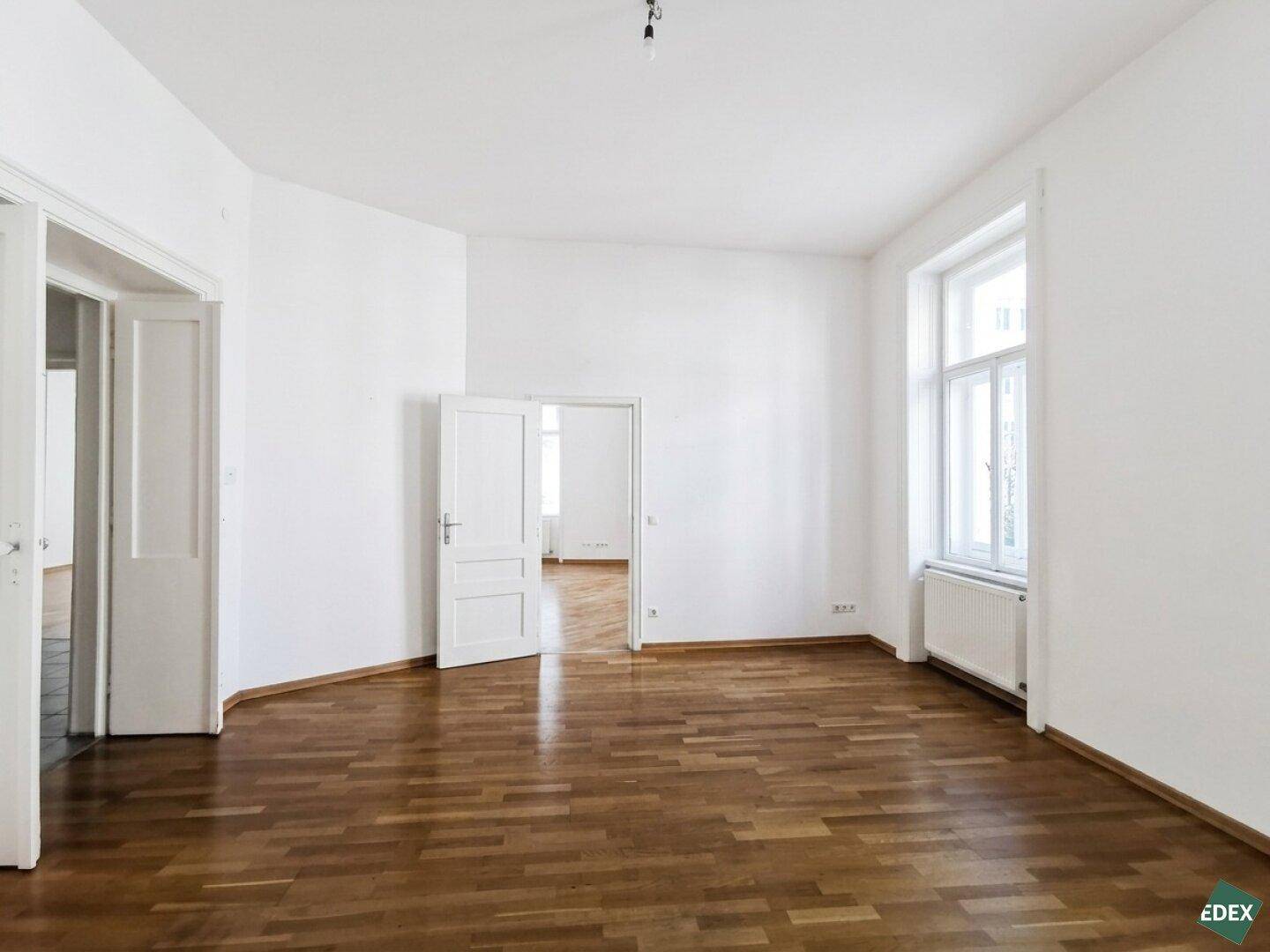 Heller Raum mit Holzboden und zwei offenen Türen, die zu weiteren Zimmern führen.