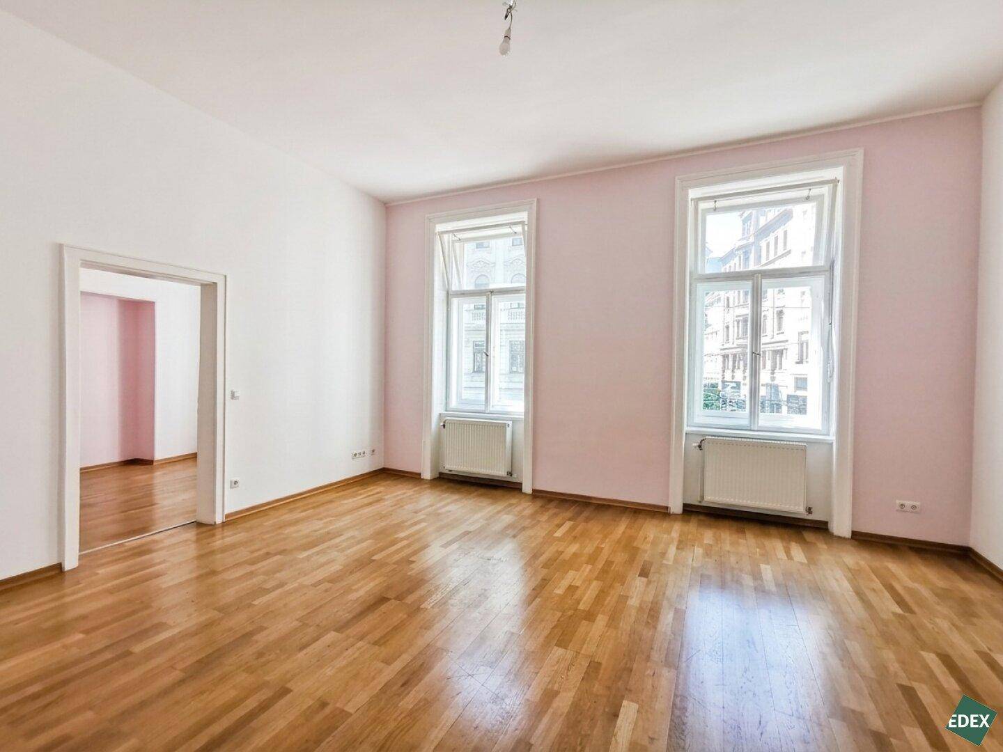 Heller Raum mit rosa Wänden, Holzboden und zwei großen Fenstern, die viel Licht spenden.