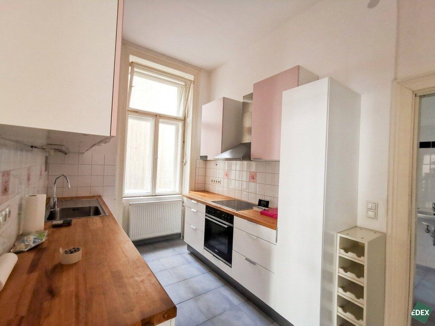 Moderne Küche mit weißen Schränken, Holz-Arbeitsplatte und einem Fenster über der Spüle.