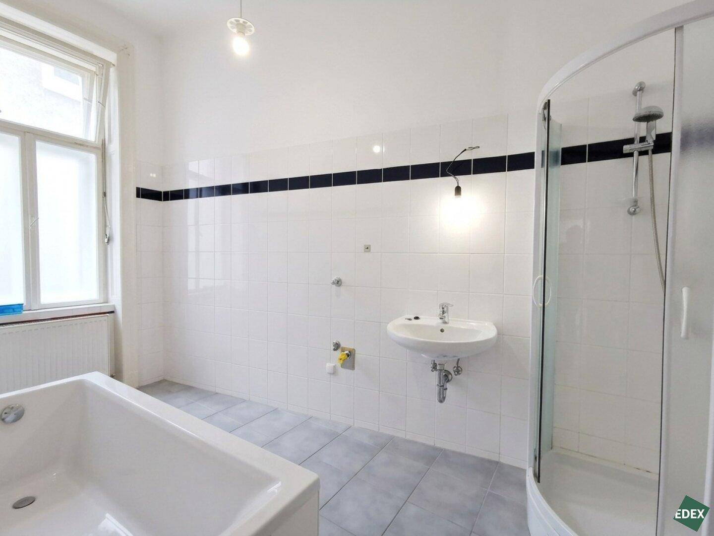 Helles Badezimmer mit Badewanne, Duschkabine, Waschbecken und einem Fenster für Tageslicht.