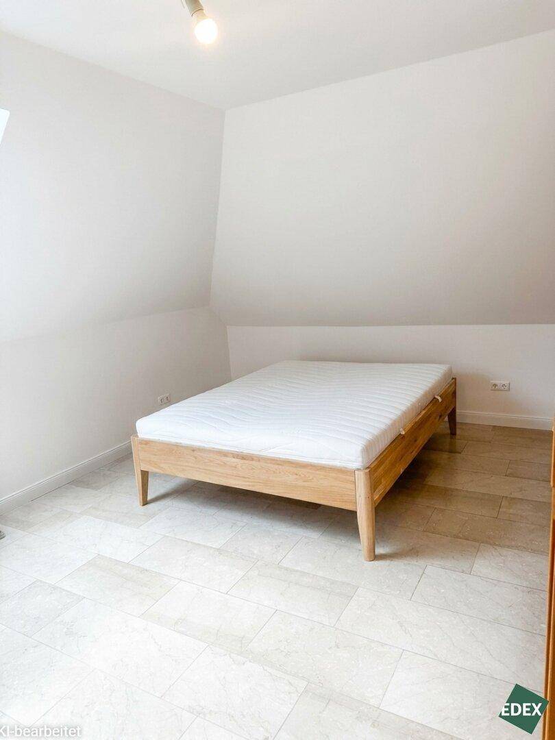 Helles Schlafzimmer im Dachgeschoss mit Holzbett und hellen Fliesenboden.