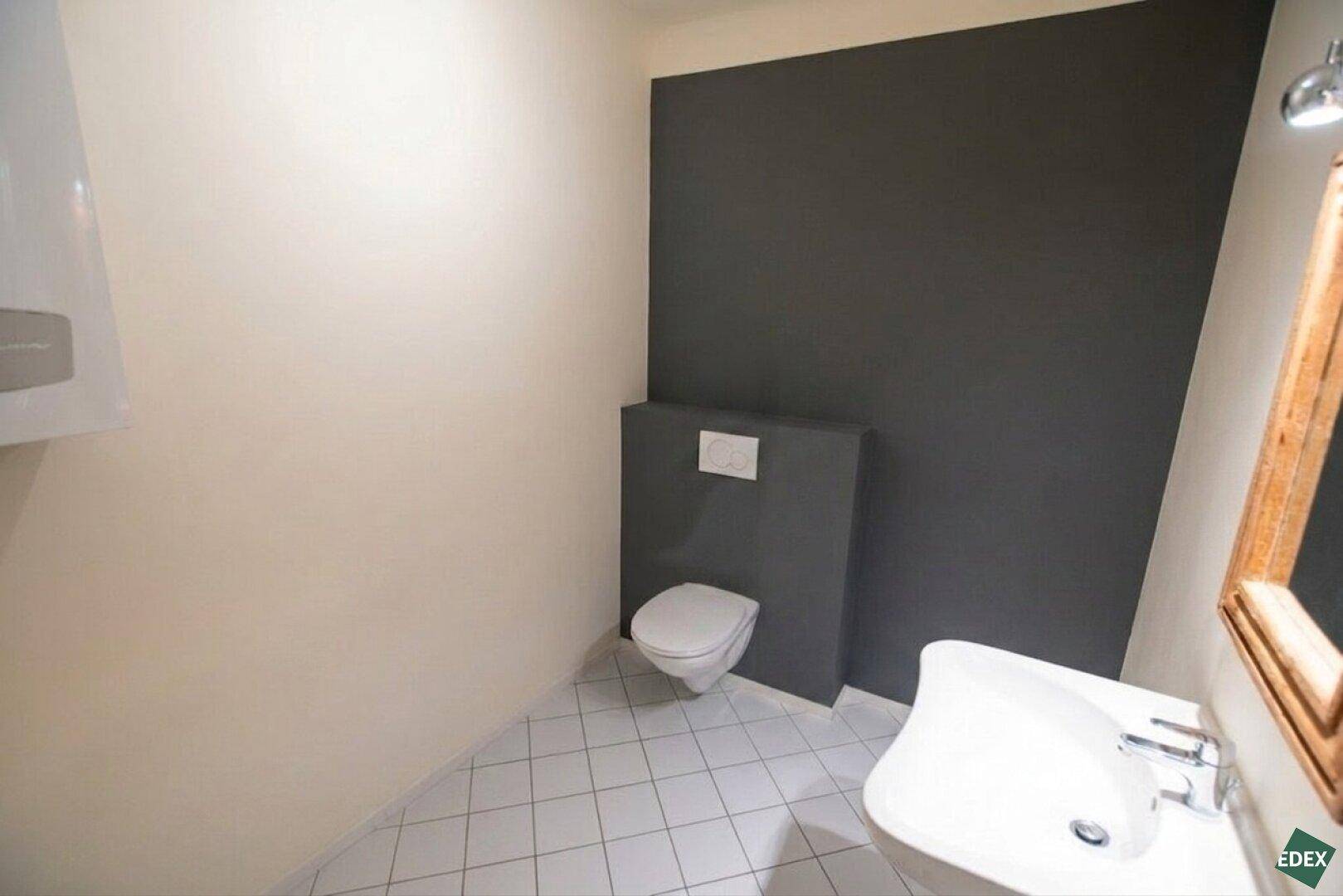 Modernes Gäste-WC mit wandhängender Toilette, Waschbecken und einer dunkelgrauen Akzentwand.