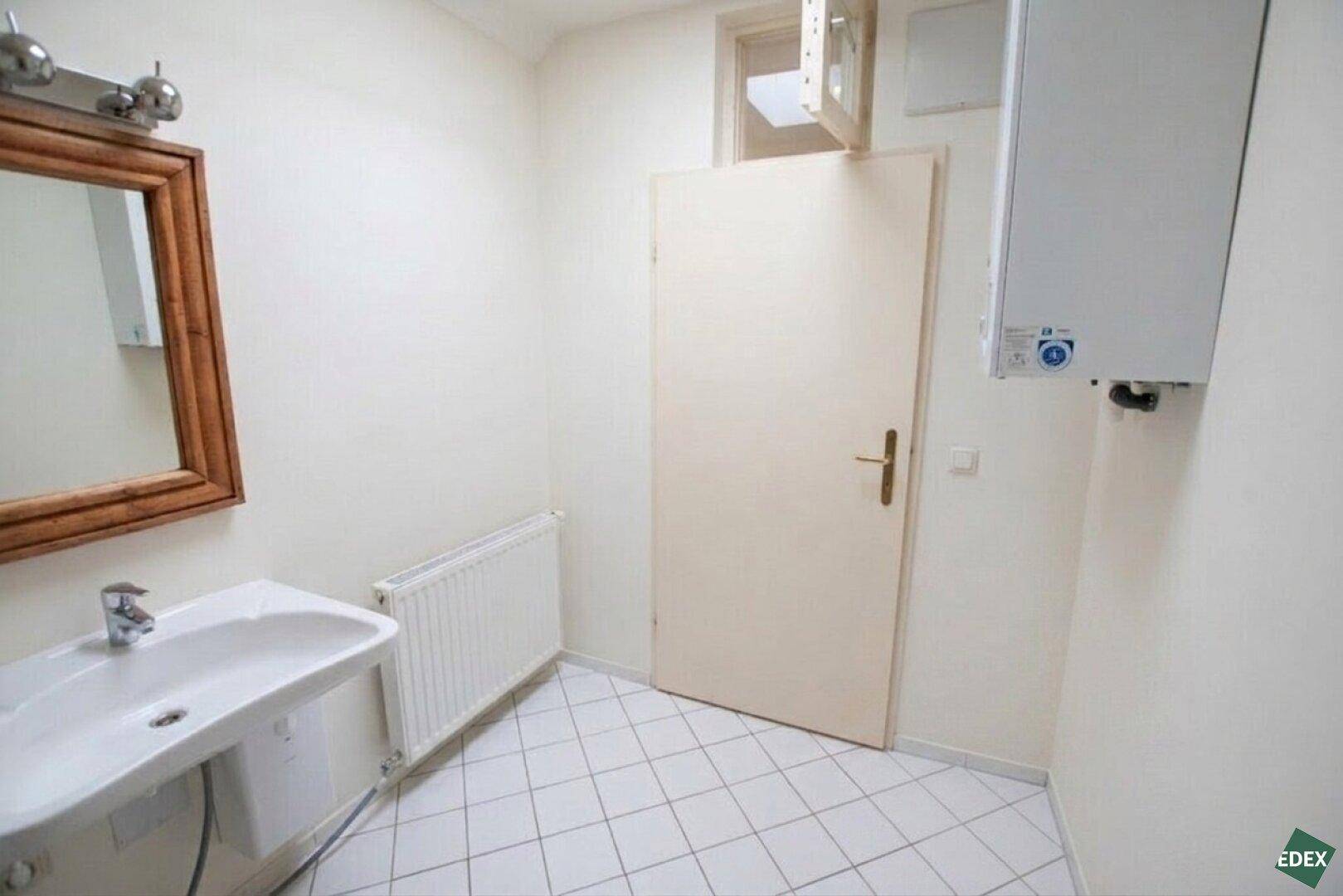 Gäste-WC mit Waschbecken, Spiegel und einem Heizkörper, die Wände sind hell gestrichen.