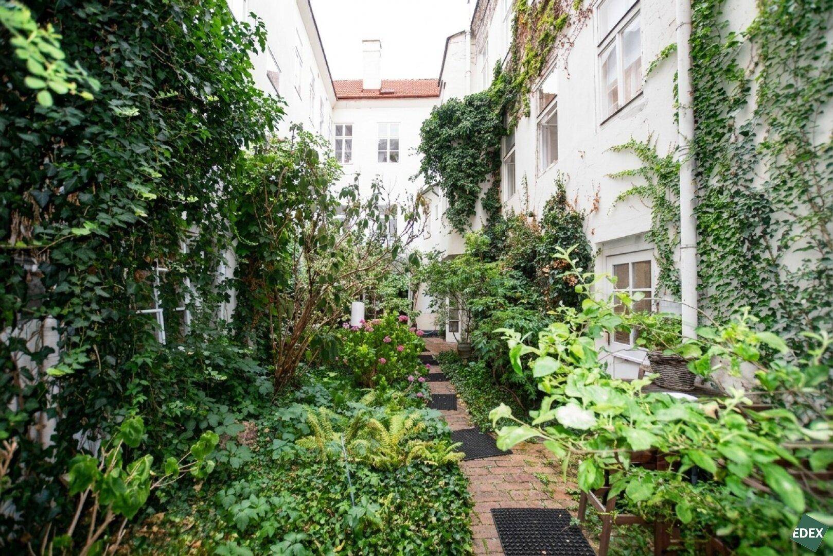 Verwinkelter Innenhof mit viel Grün, Efeu an den Fassaden und einem charmanten Weg.