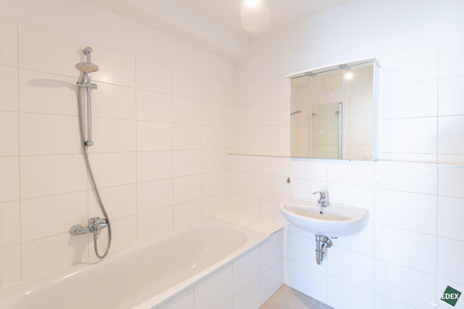 Gefliestes Badezimmer mit Badewanne, Waschbecken und Spiegelschrank, in hellem und sauberem Zustand.