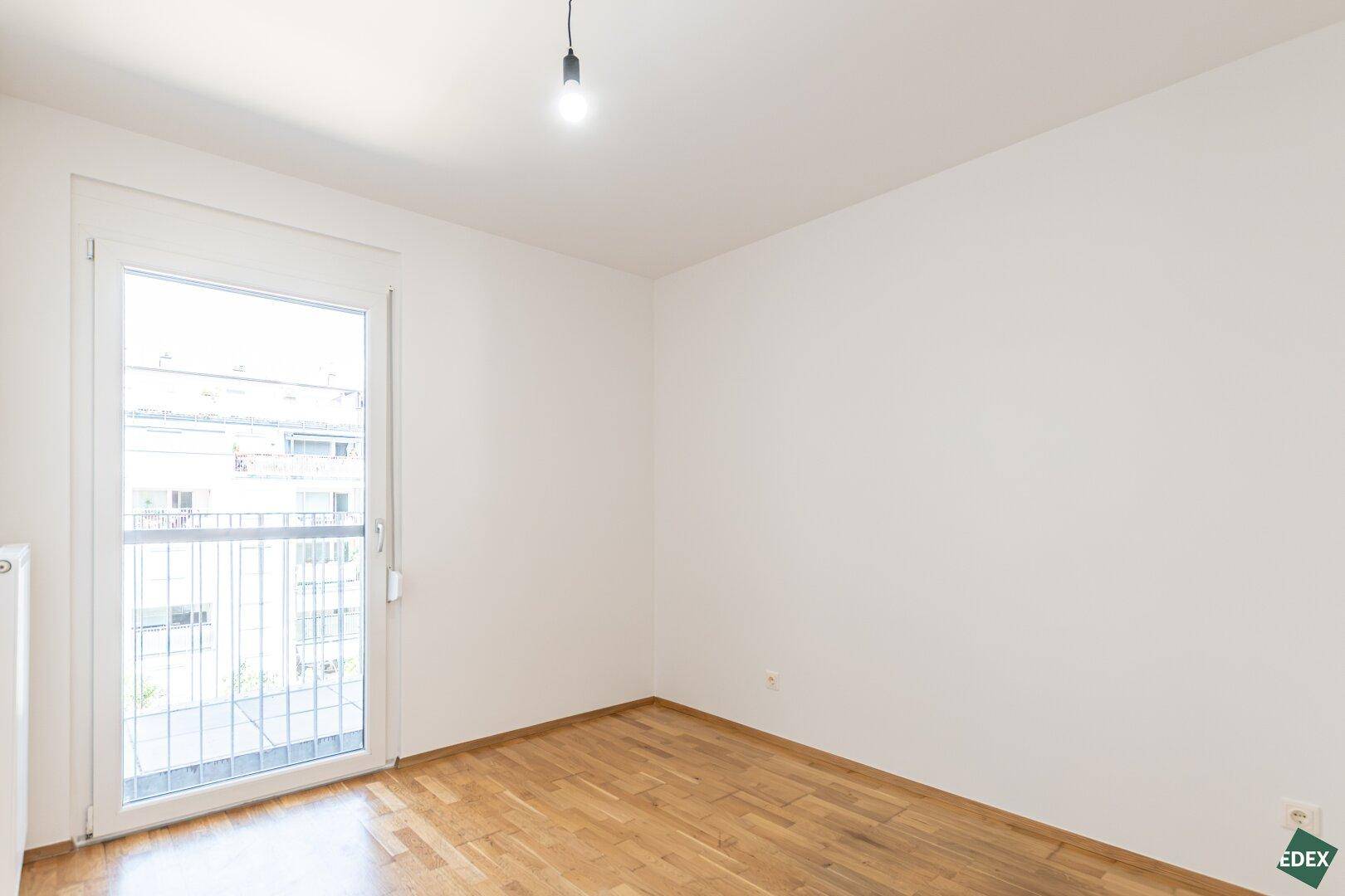 Helles Schlafzimmer mit Parkettboden und Zugang zu einem französischen Balkon, der viel Licht spendet.