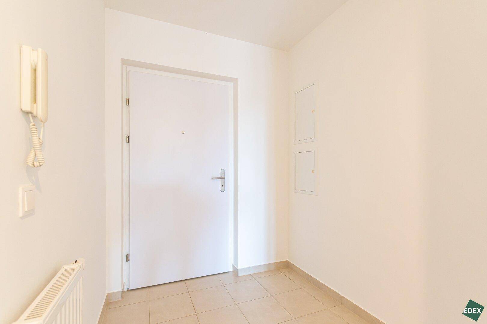 Eingangsbereich mit Fliesenboden, Gegensprechanlage und Heizkörper, der zur Wohnungstür führt.