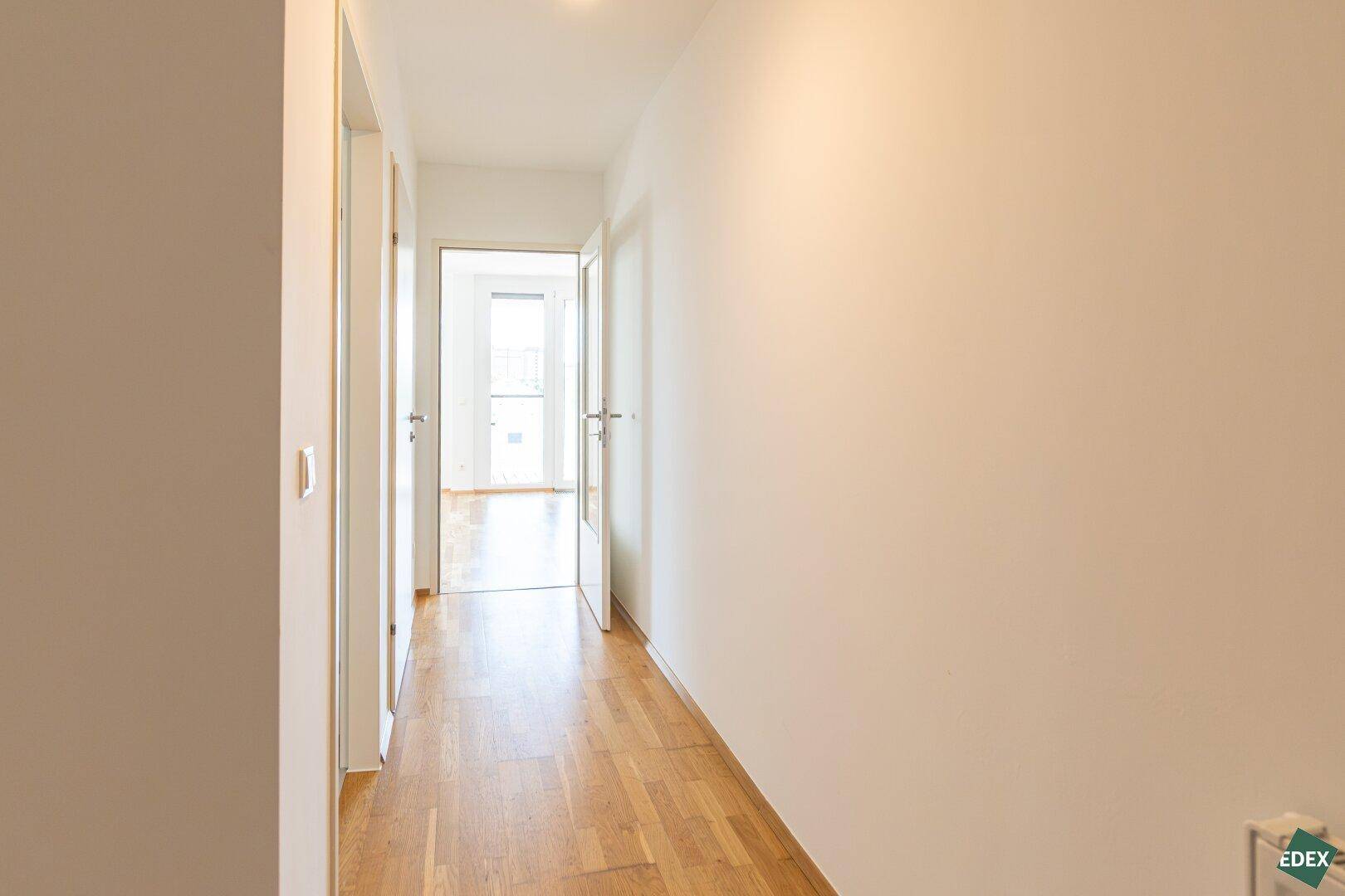 Langer, heller Flur mit Parkettboden, der verschiedene Bereiche der Wohnung miteinander verbindet.
