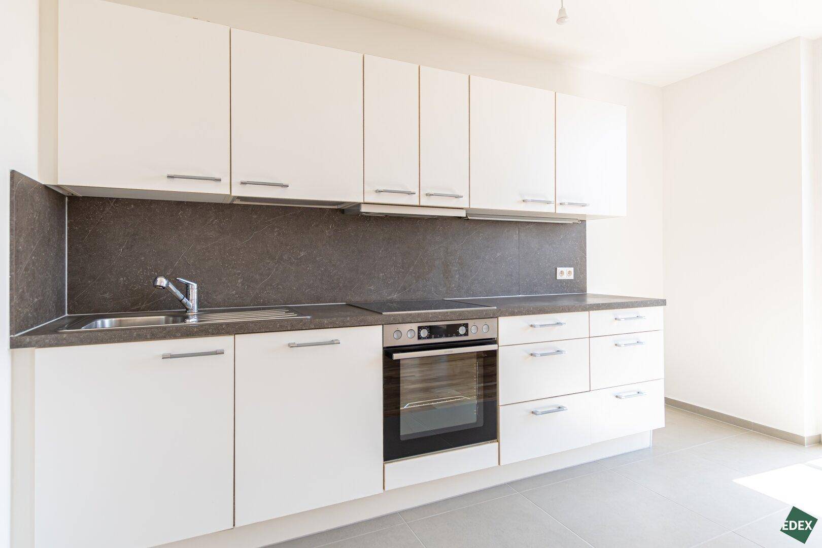 Moderne Einbauküche mit weißen Schränken, dunkler Arbeitsplatte und integriertem Backofen.