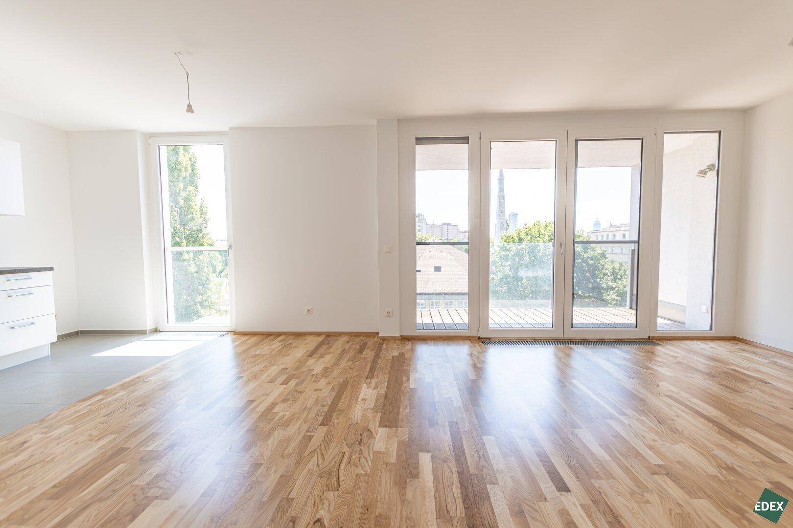 Lichtdurchfluteter Wohnbereich mit Holzboden und großen Fenstern, die viel Tageslicht hereinlassen.