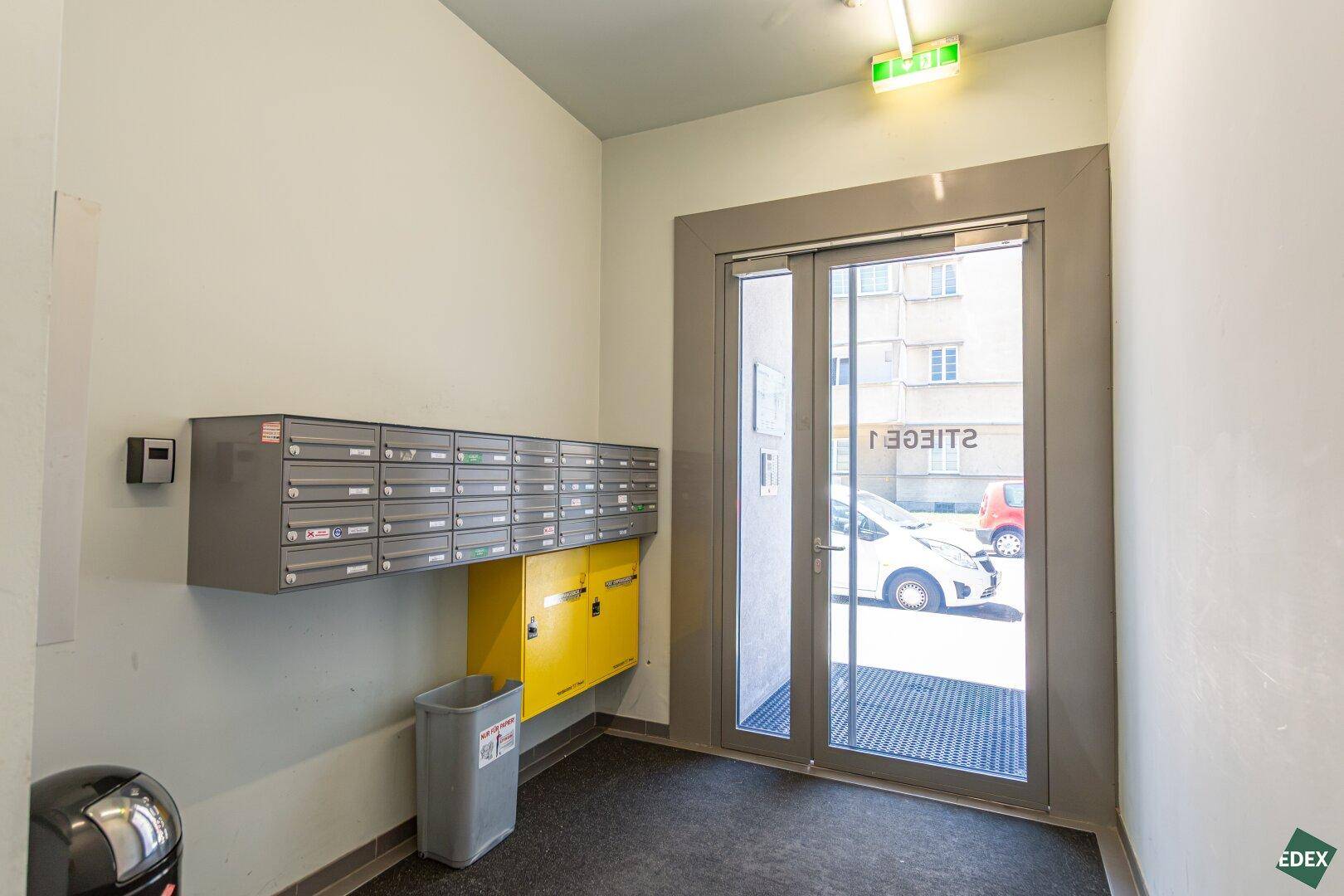 Eingangsbereich des Gebäudes mit Briefkästen und Zugang zur Straße, hell und funktional gestaltet.