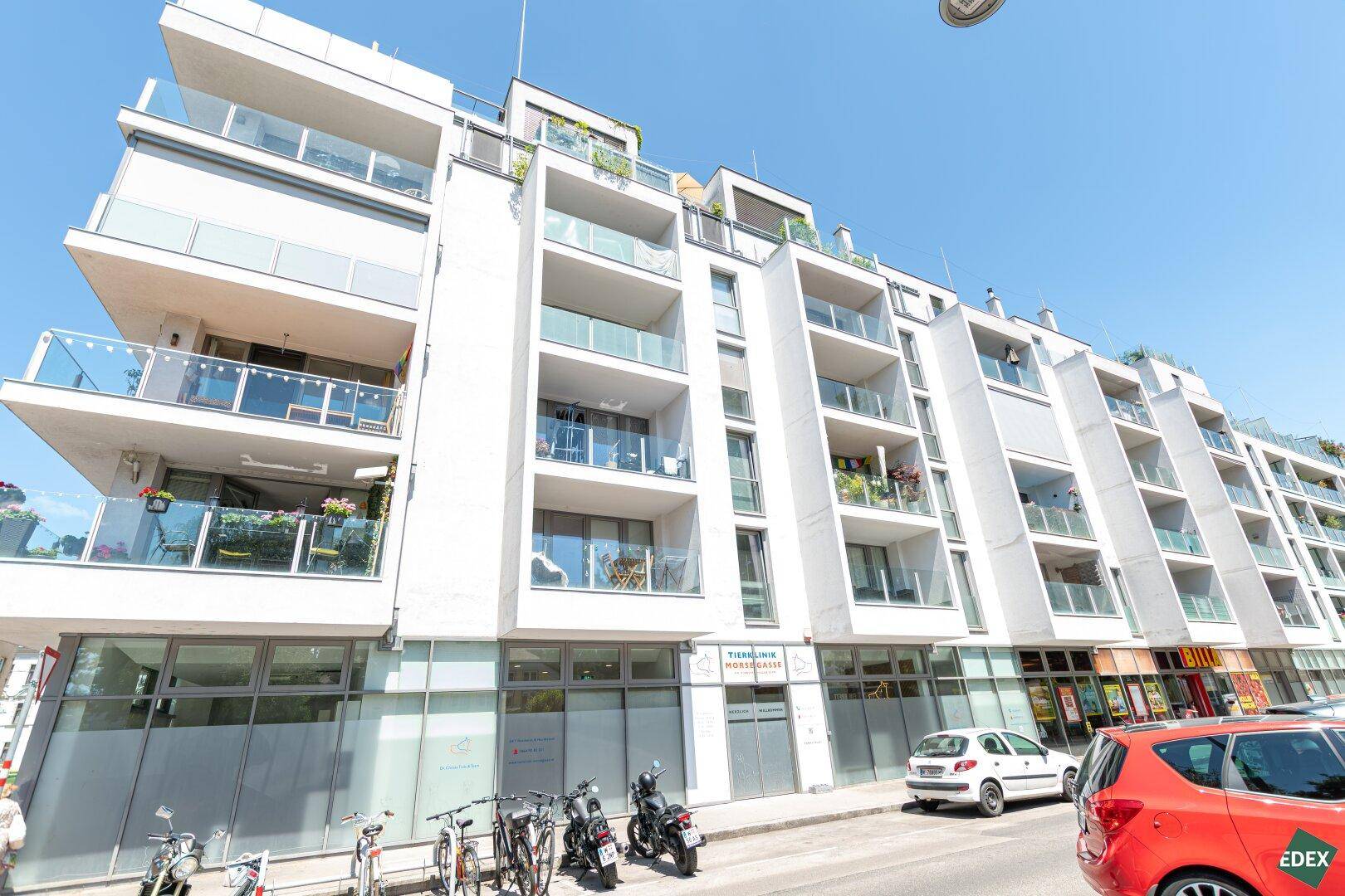 Moderne Wohnanlage mit mehreren Balkonen und großen Fenstern, gelegen an einer städtischen Straße.