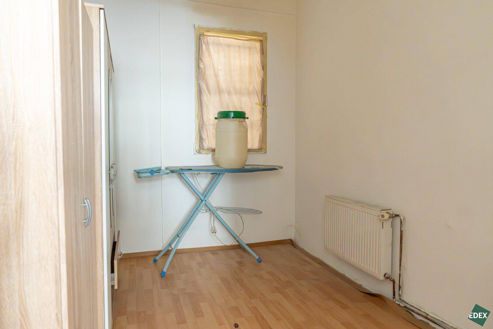 Kleiner Raum mit Bügelbrett, Heizkörper und einem Fenster, ideal als Hauswirtschaftsraum.