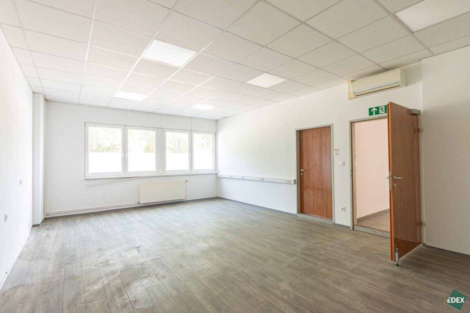 Heller Büroraum mit großen Fenstern, modernem Vinylboden und Klimaanlage, ideal für Teams.