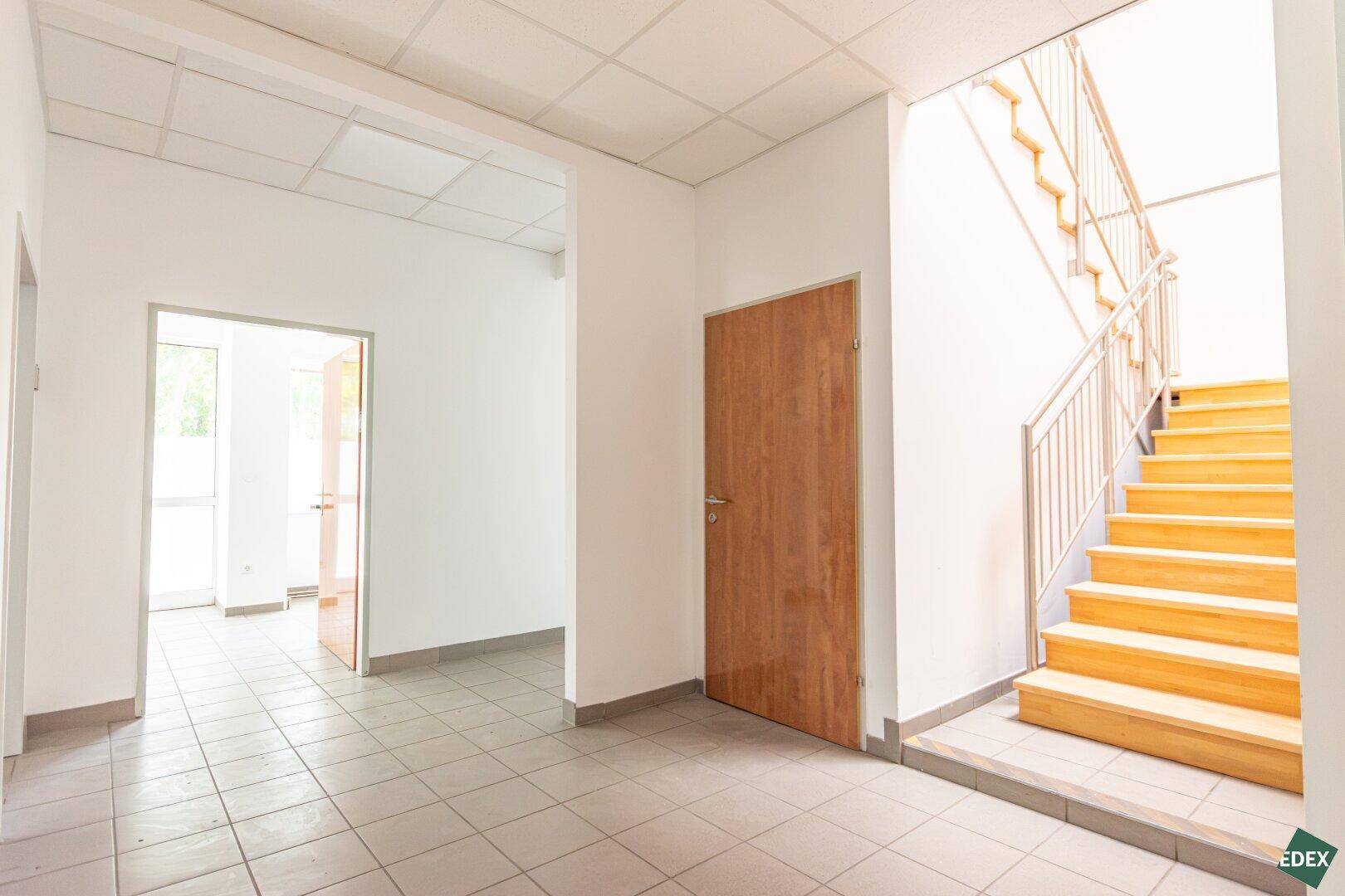 Flur mit Fliesenboden und Holztreppe, die zu den oberen Etagen führt, mit mehreren Türen.