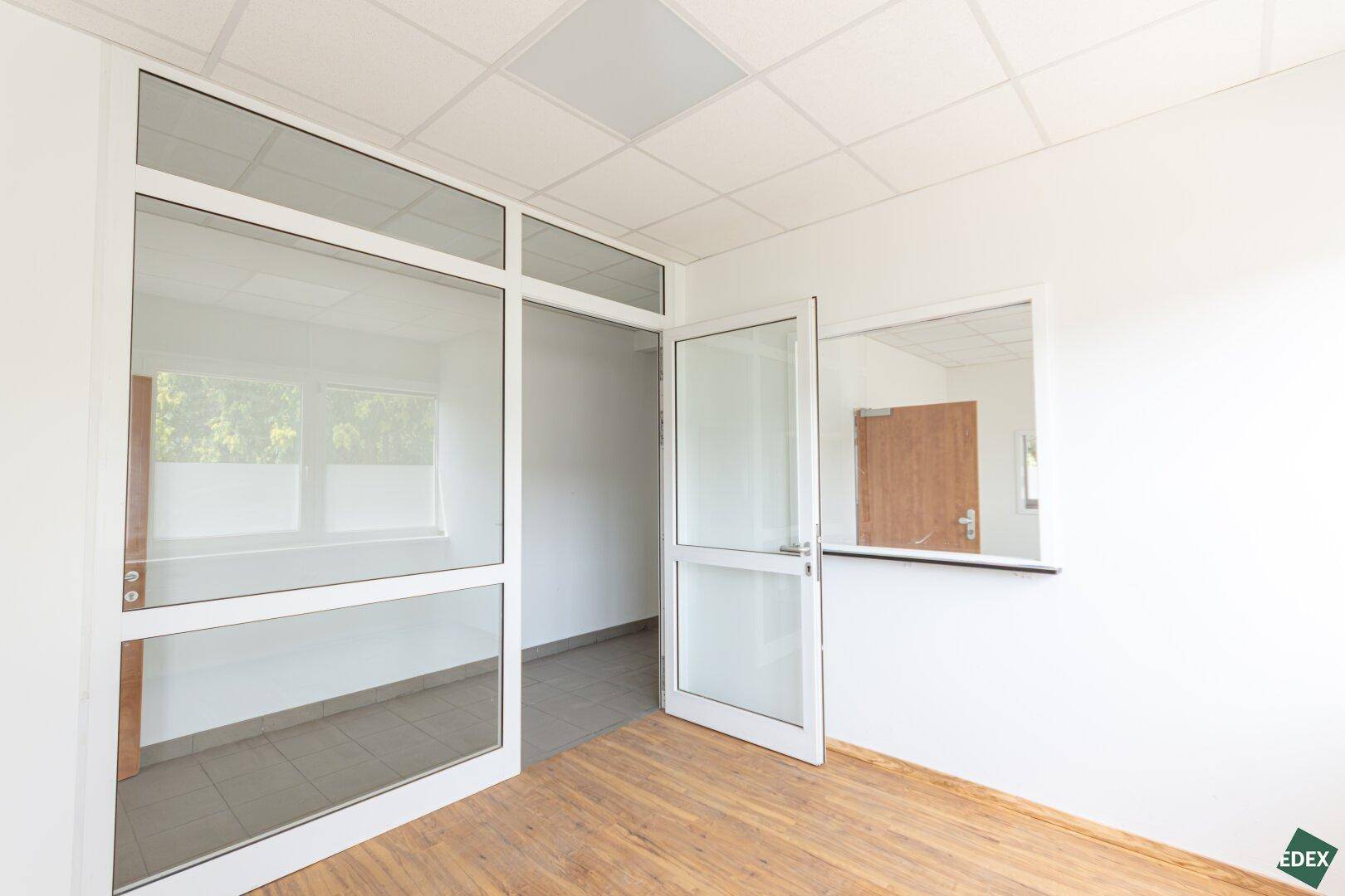 Büroraum mit Laminatboden und Glaswand, die für eine offene und helle Arbeitsatmosphäre sorgt.