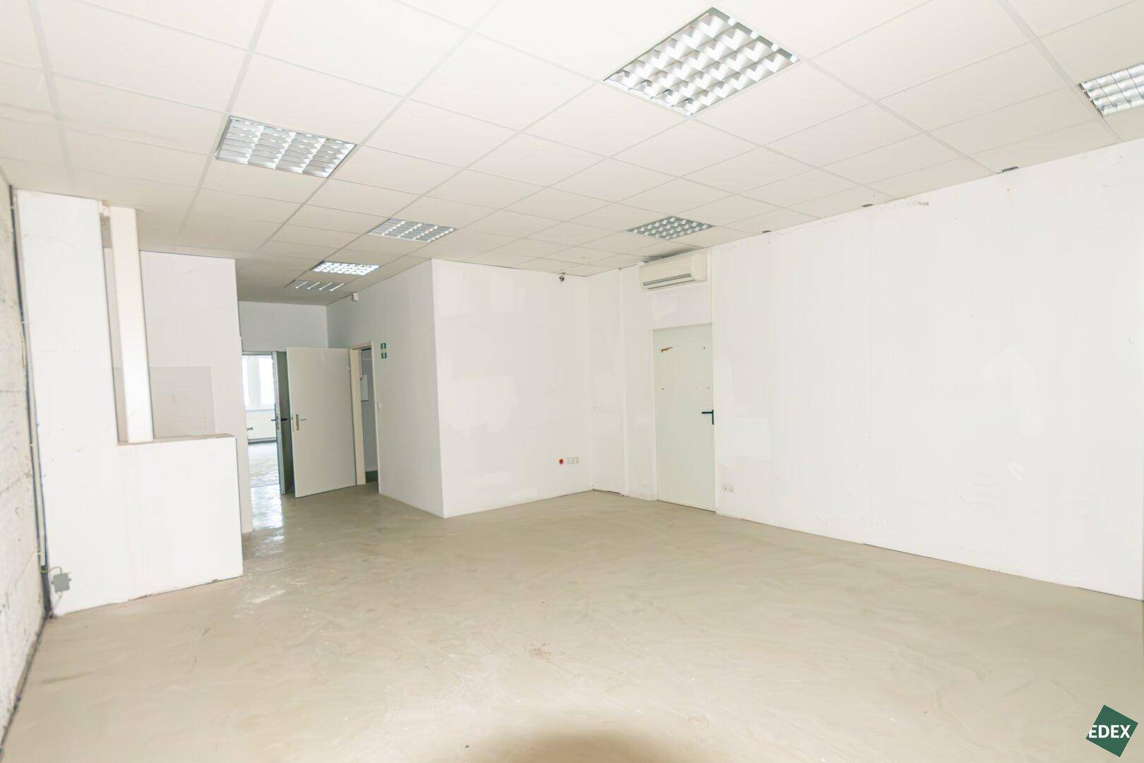 Großer, leerer Büroraum mit Klimaanlage, abgehängter Decke und mehreren Türen.