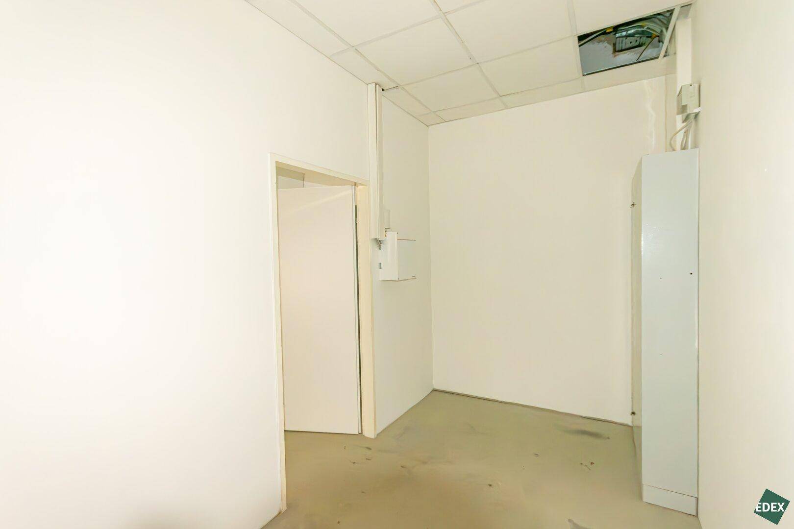 Kleiner Büroraum mit weiß gestrichenen Wänden, Betonboden und einem Schrank.