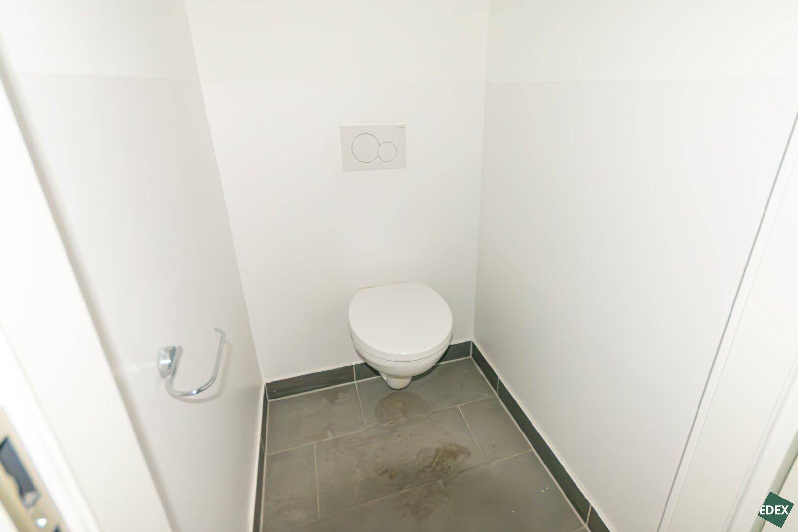 Separate Toilette mit dunklem Fliesenboden und weiß gestrichenen Wänden.
