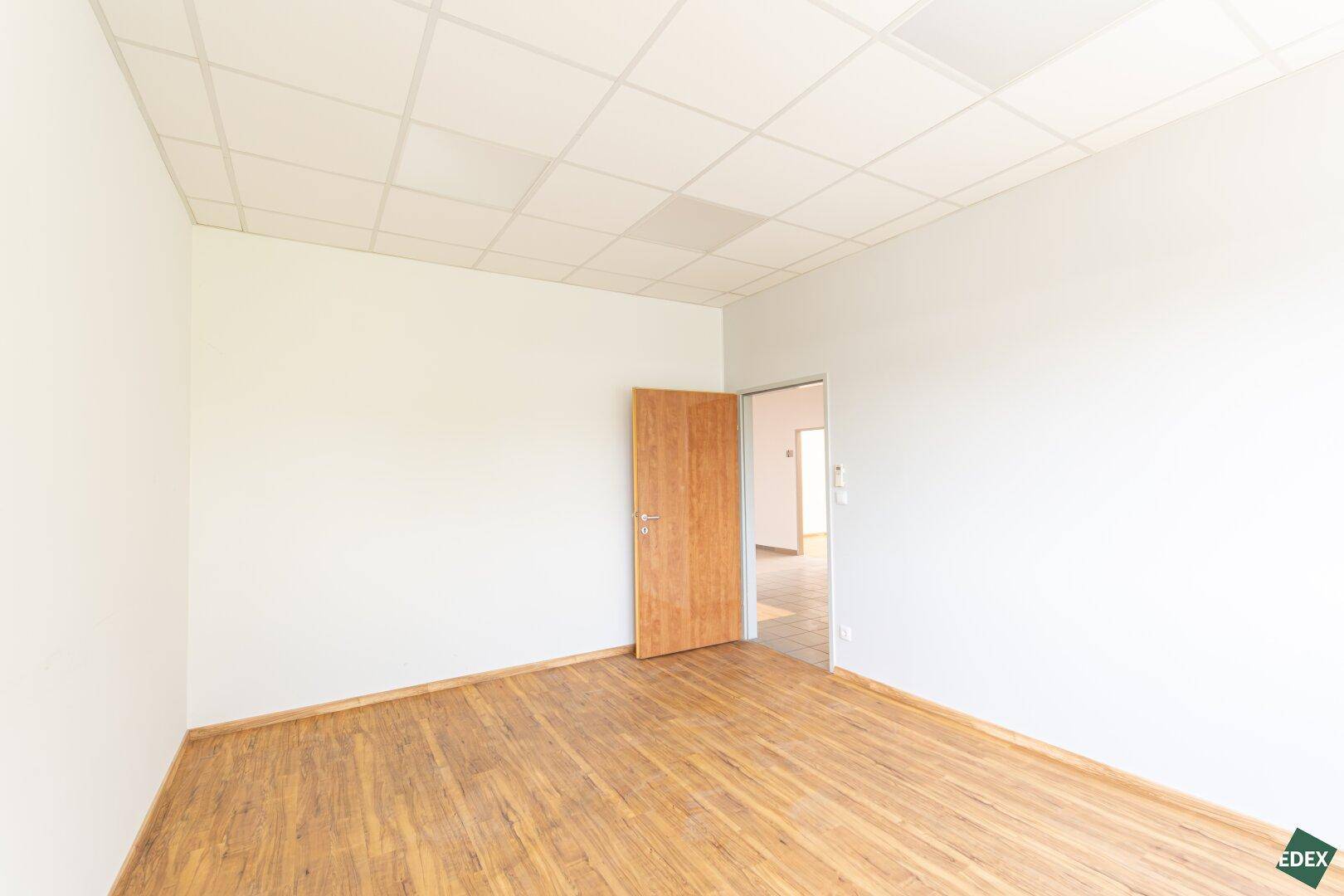 Leerer Büroraum mit Laminatboden und Holztür, bereit zur individuellen Gestaltung und Nutzung.