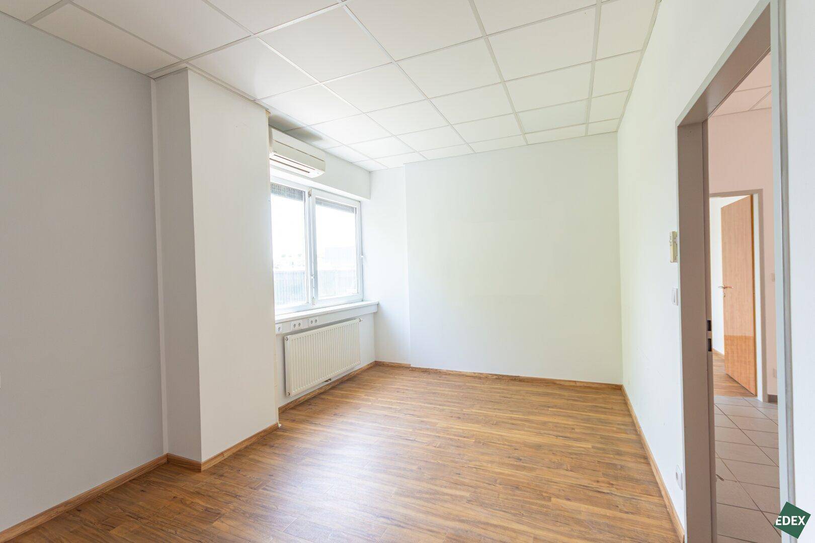Heller Büroraum mit Laminatboden, Fenster und Klimaanlage, ideal für ein Einzelbüro.