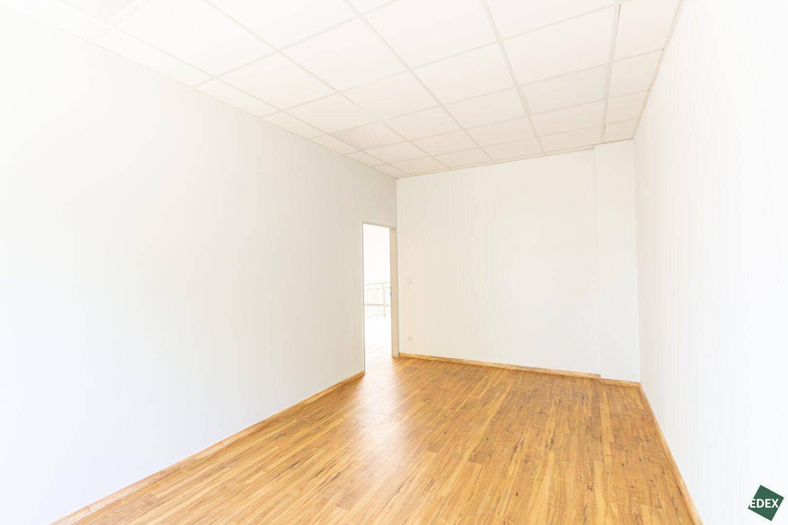 Leerer Büroraum mit hellem Laminatboden und einer abgehängten Decke, bereit zur individuellen Gestaltung.