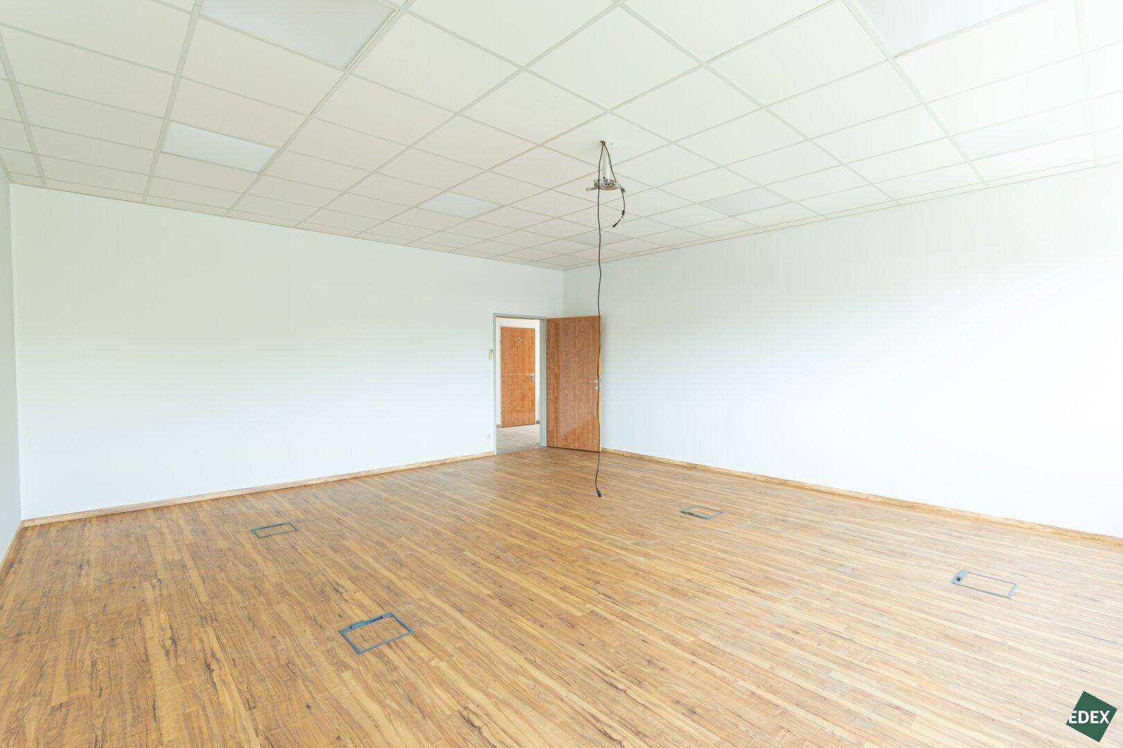 Geräumiger Büroraum mit Laminatboden, abgehängter Decke und Bodentanks für flexible Arbeitsplatzgestaltung.