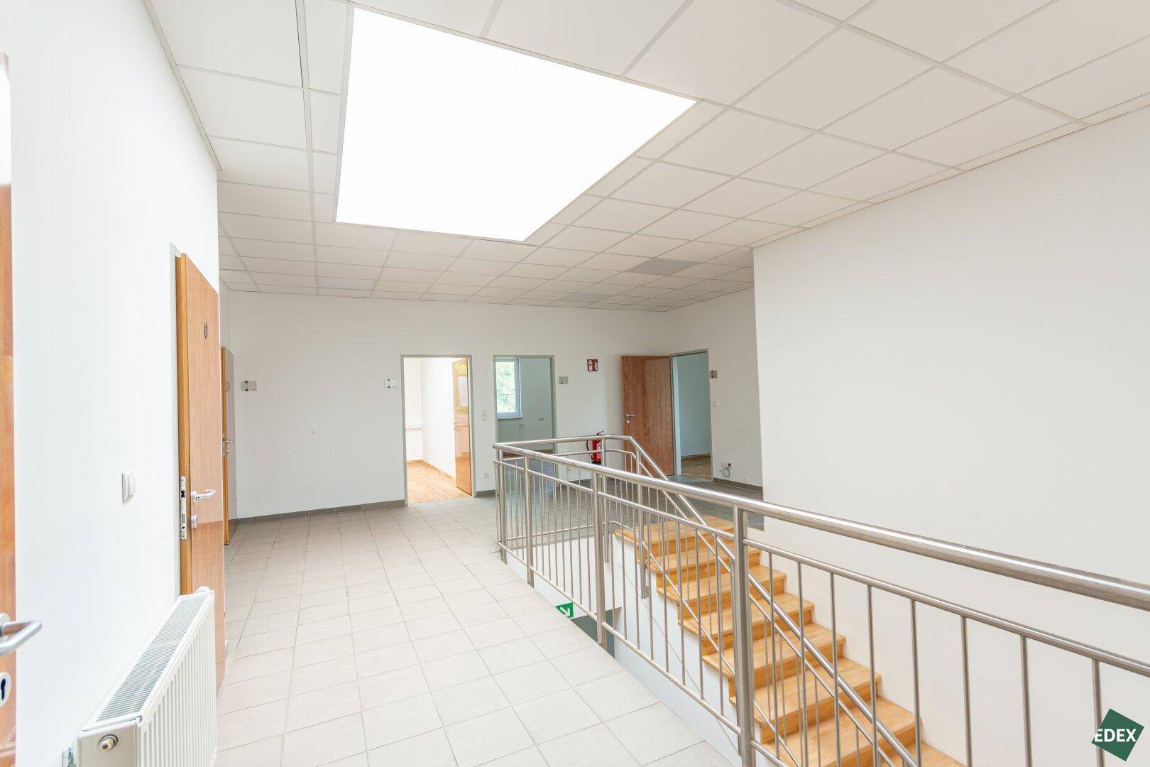 Geräumiger Flur mit Fliesenboden und Treppe mit Edelstahlgeländer, der zu weiteren Räumen führt.