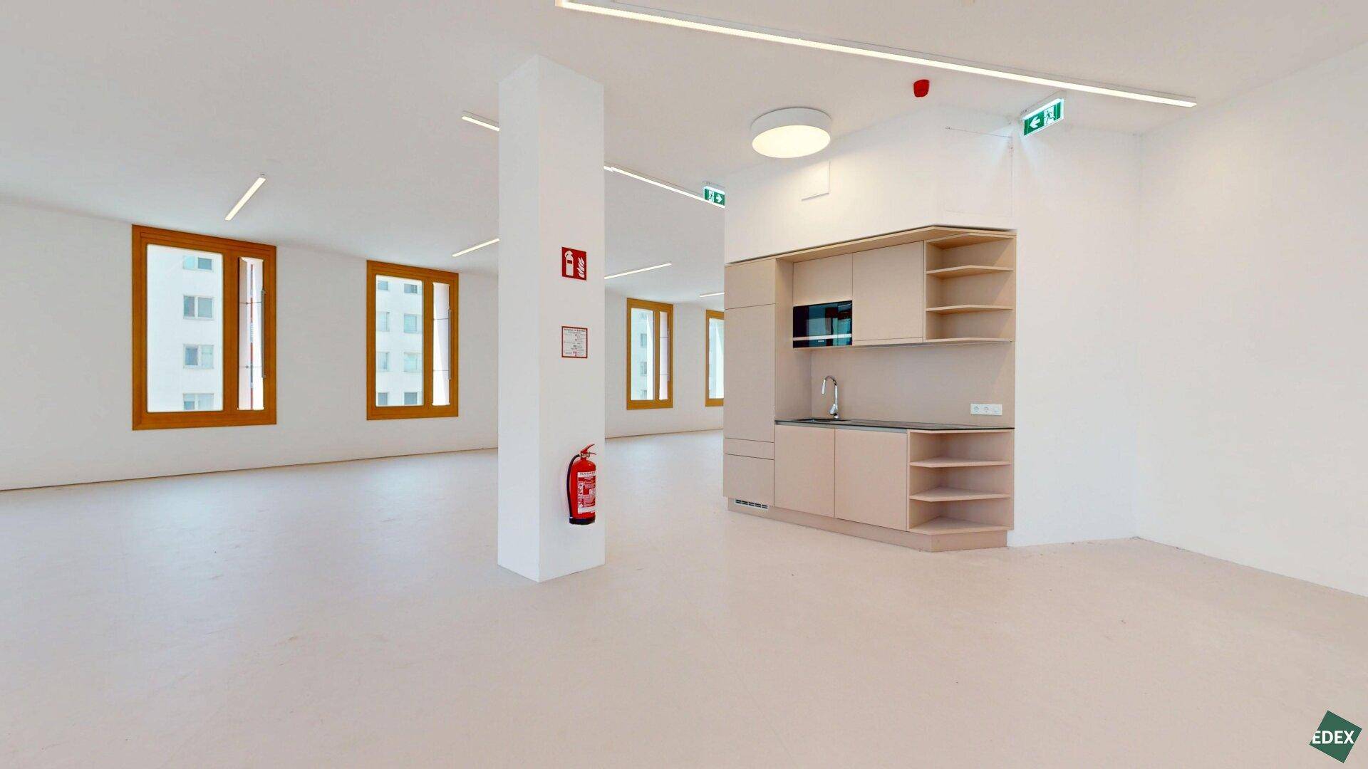 Moderner Büroraum mit integrierter Küchenzeile, Mikrowelle und vielen Fenstern für natürliches Licht.
