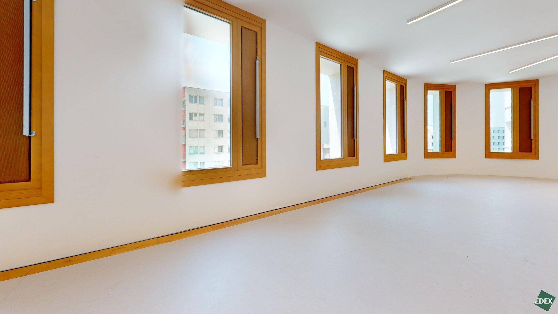 Detailansicht eines hellen Gewerberaums mit Holzfenstern und Blick auf umliegende Gebäude.