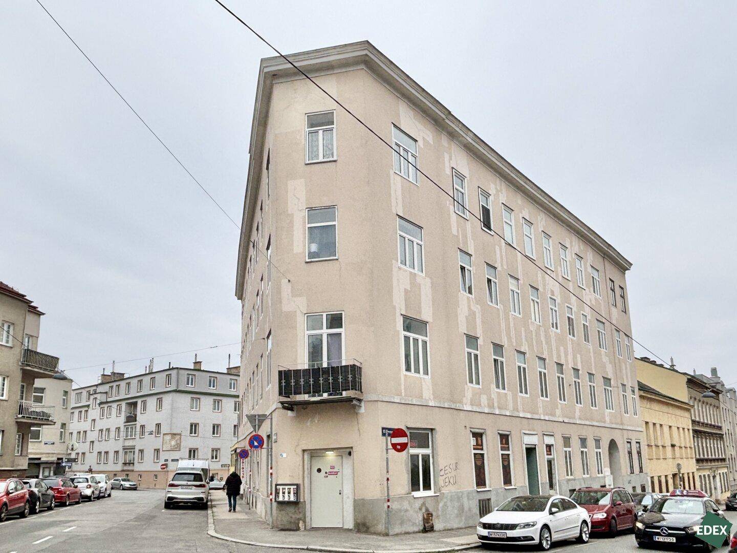 Eckgebäude in städtischer Umgebung mit klassischer Fassade und vielen Fenstern.