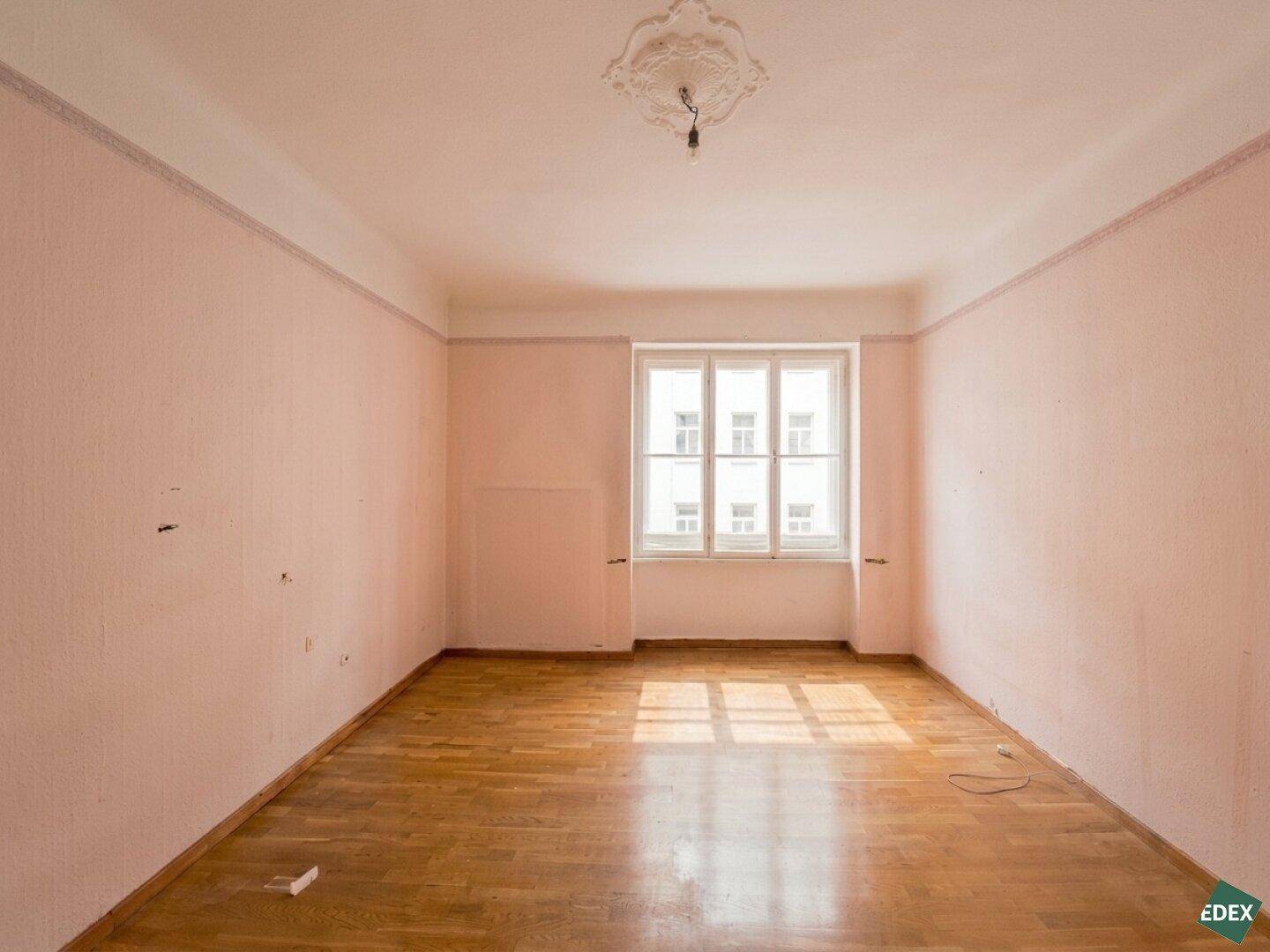 Geräumiges, unmöbliertes Wohnzimmer mit Parkettboden und großen Fenstern, bereit zur individuellen Gestaltung.