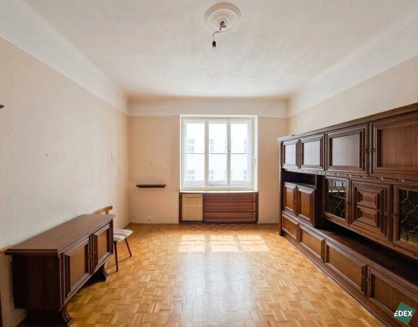Geräumiges Wohnzimmer mit traditionellen Holzmöbeln, Parkettboden und großen Fenstern.