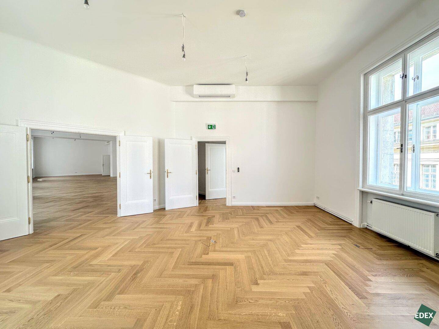 Heller Büroraum mit elegantem Fischgrätparkett, weißen Türen und Klimaanlage, bereit zum Bezug.