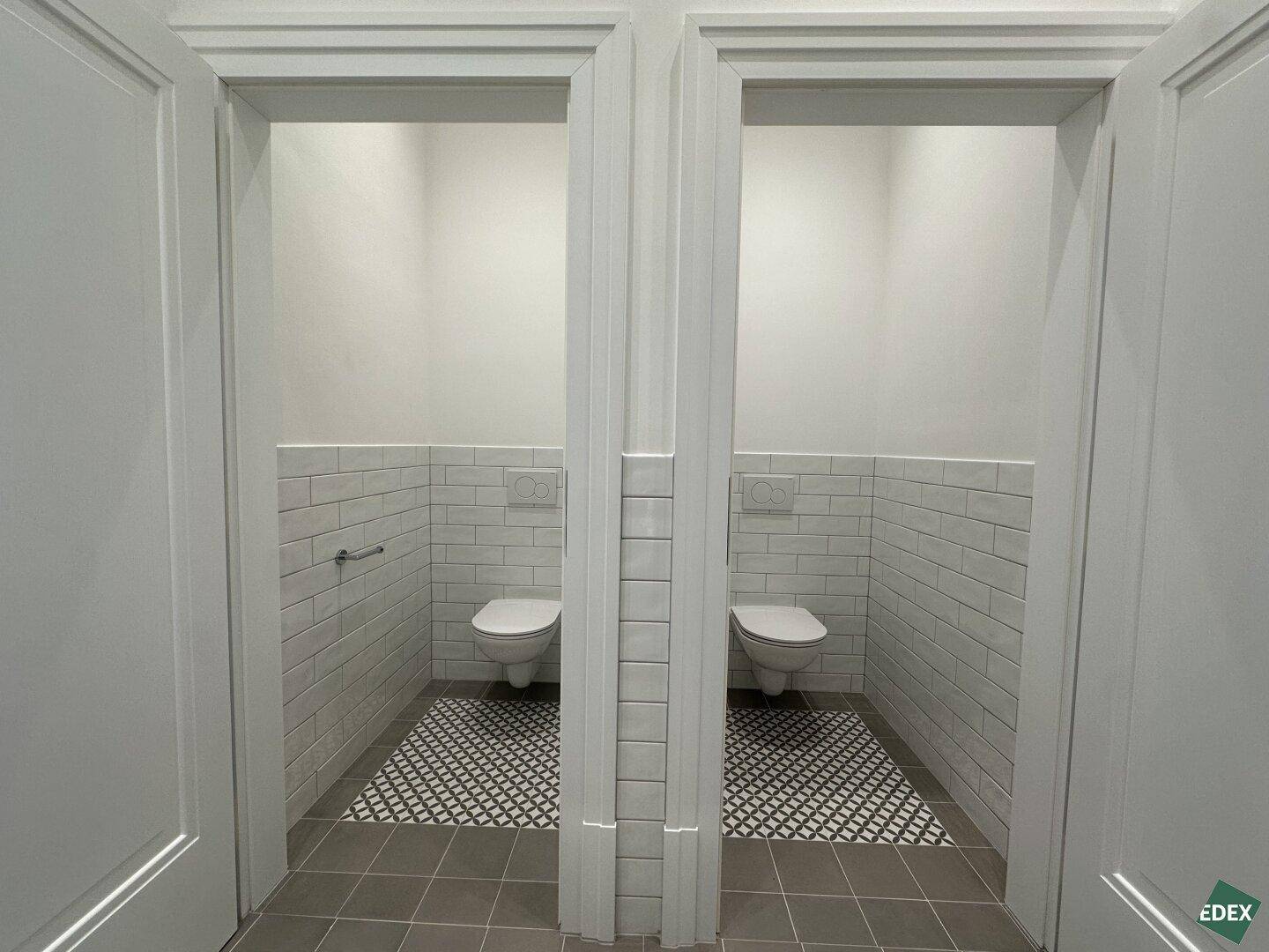 Zwei separate Toilettenräume mit modernen Wand-WCs und stilvollen gemusterten Bodenfliesen.