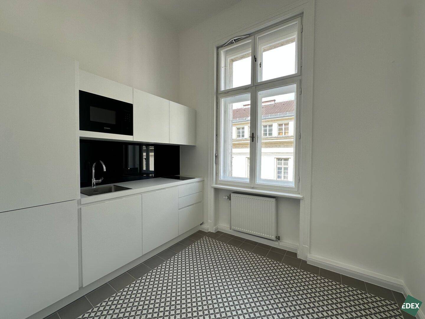 Moderne Küchenzeile mit weißen Schränken, Spüle und Mikrowelle, ergänzt durch gemusterte Fliesen.